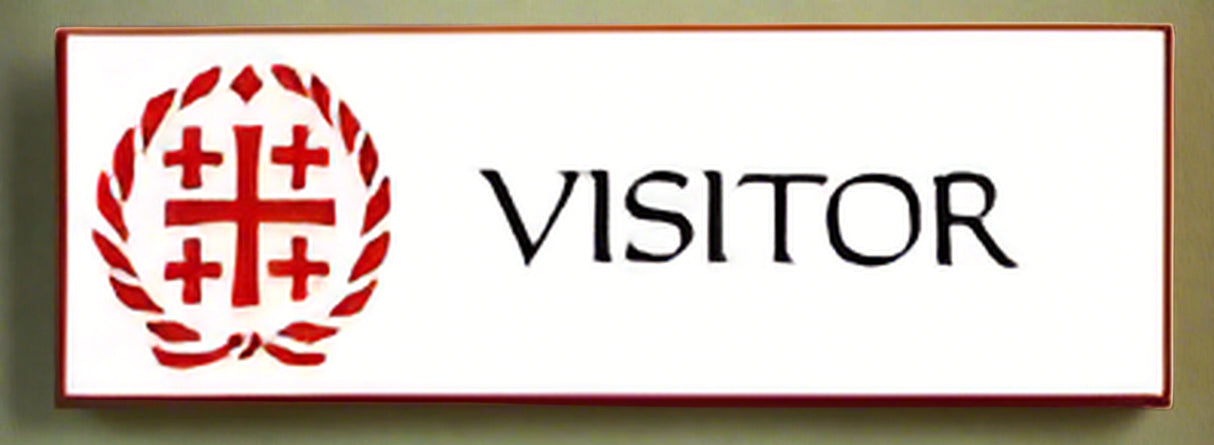 A badge with a white background and red text that reads 'VISITOR' and a small red cross above the text.